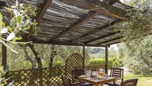 A wooden pergola with a table and chairs, surrounded by a lattice fence and lush greenery. - Le Buche by Interhome (Castellina in Chianti)
