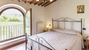 A bedroom with a bed, a window with a view of greenery, a radiator, and a ceiling with exposed beams. - Le Buche by Interhome (Castellina in Chianti)