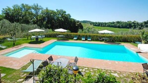 A rectangular swimming pool with a tiled deck, surrounded by lounge chairs and umbrellas. - Le Buche by Interhome (Castellina in Chianti)