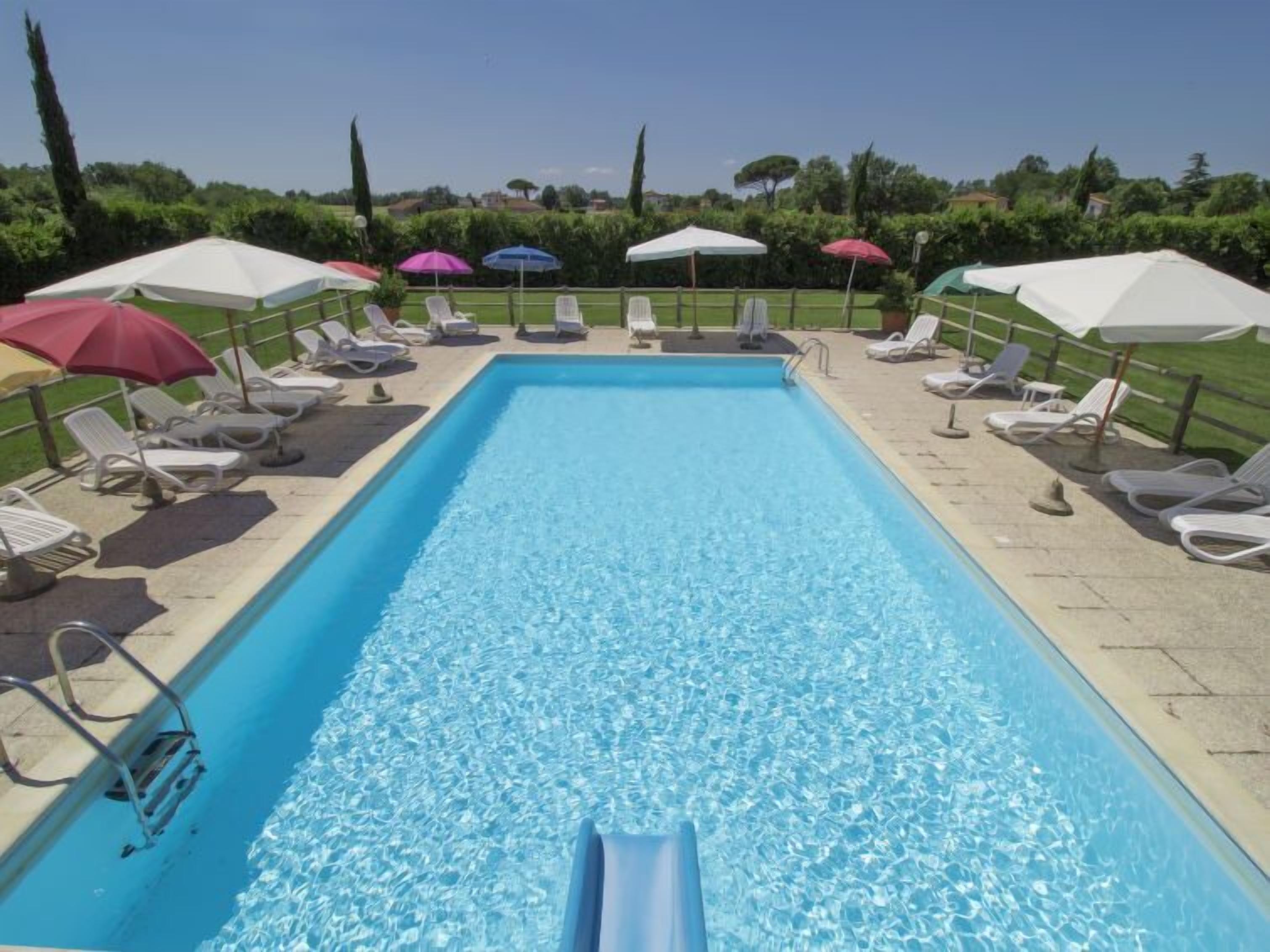 A rectangular swimming pool with clear water, surrounded by lounge chairs and umbrellas.