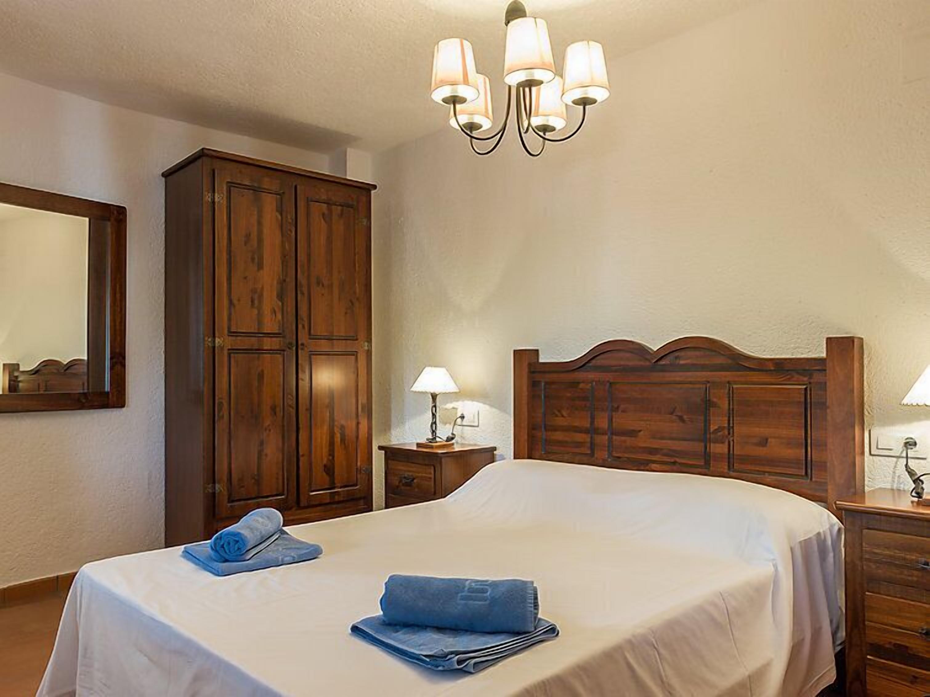 A hotel room with a large bed, wooden wardrobe, bedside lamps, and a chandelier.