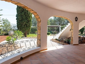 A covered patio with stone arches, a metal railing, and a view of a garden and staircase.