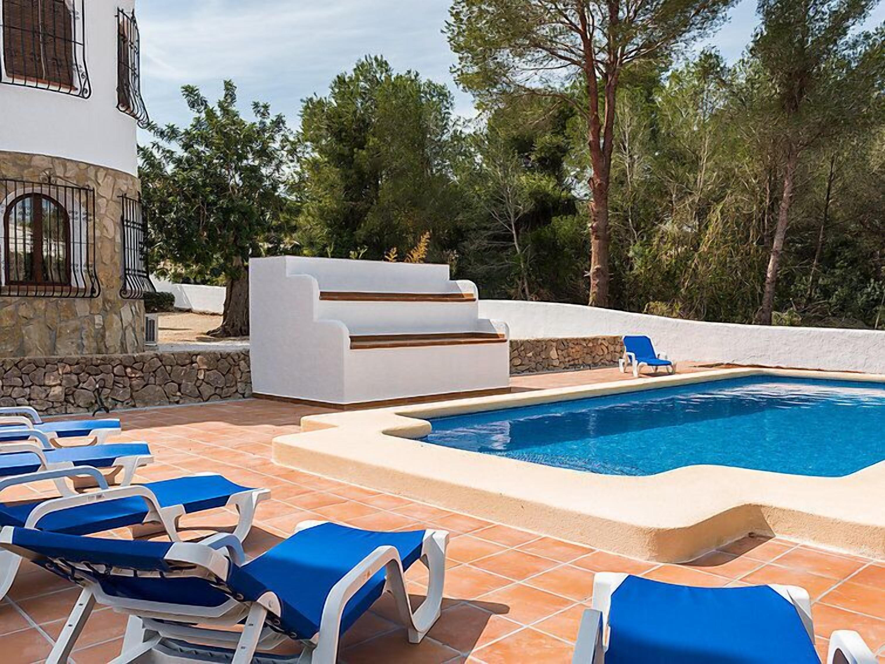 Un espace piscine avec des chaises longues bleues, un banc blanc et un mur en pierre.