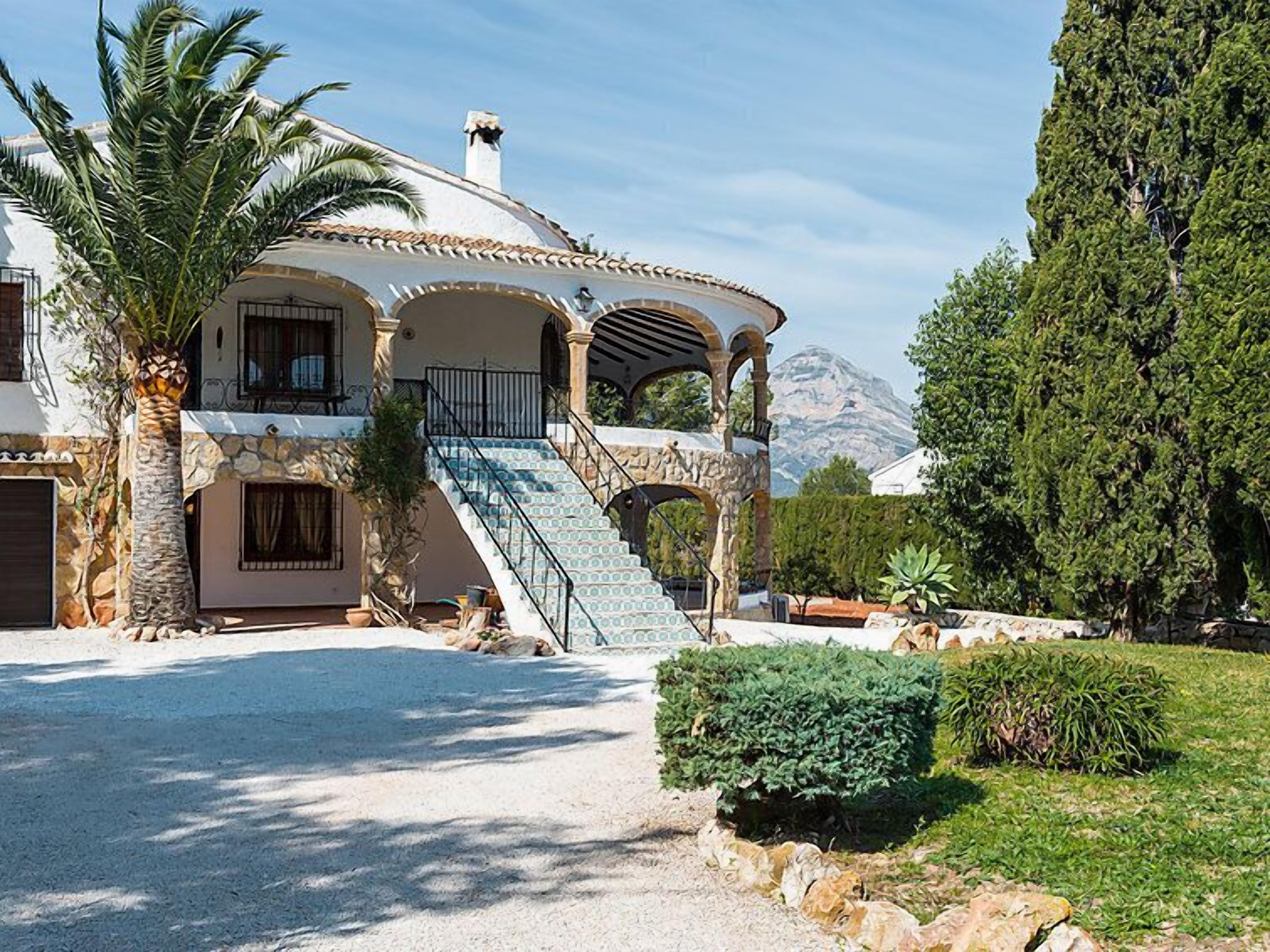 Eine mediterrane Villa mit Steinaußenwand, einer zentralen Treppe und Blick auf Berge.