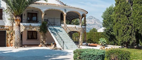 Eine mediterrane Villa mit Steinaußenwand, einer zentralen Treppe und Blick auf Berge.