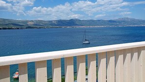 Ein Balkon mit Blick auf ein ruhiges Meer, ein Segelboot und ferne Berge.