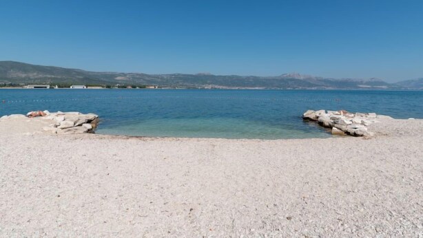 Ein Kiesstrand mit klarem Wasser und fernen Bergen.