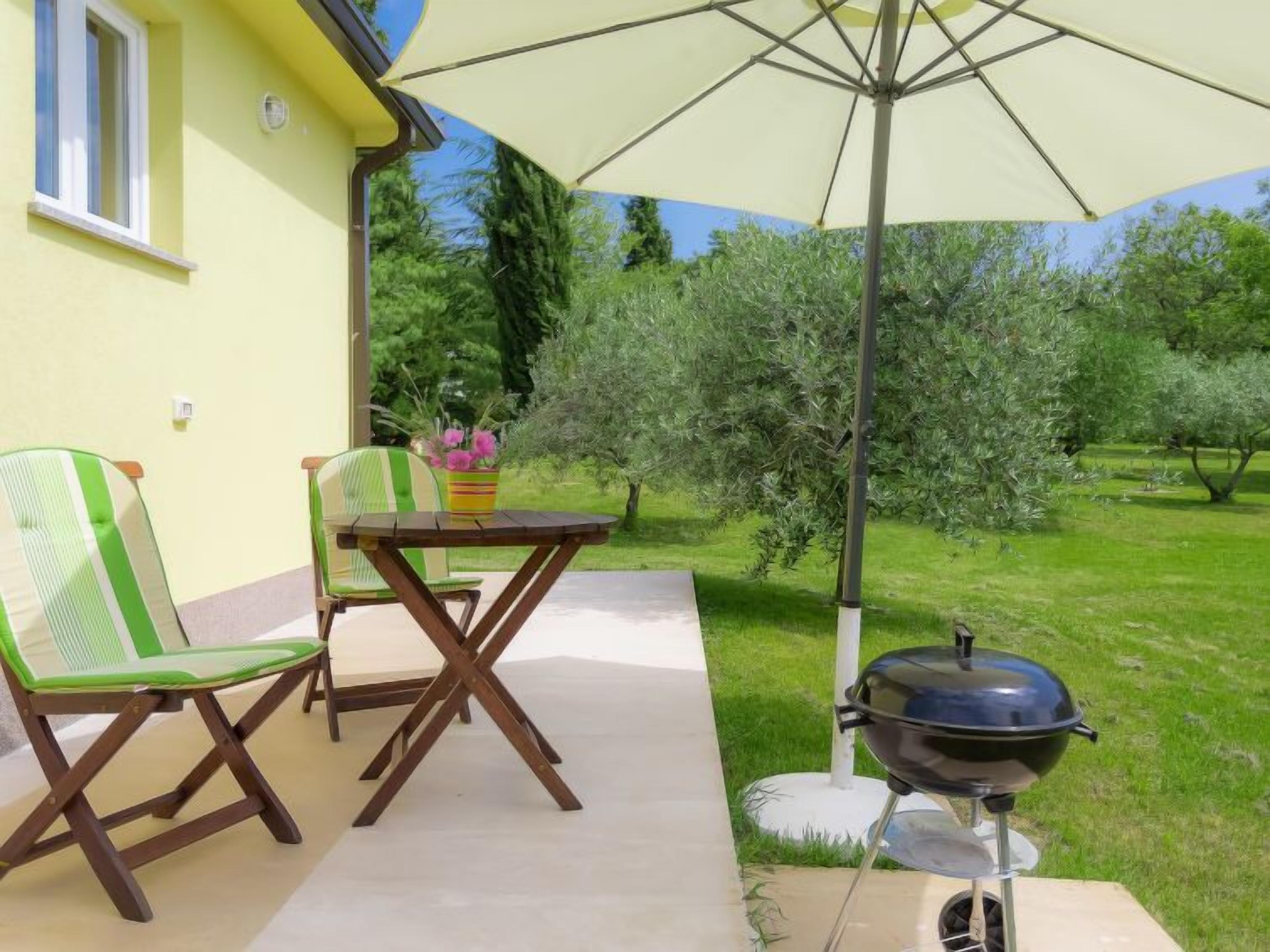 An outdoor patio with a table and chairs, a barbecue grill, and a large umbrella providing shade.