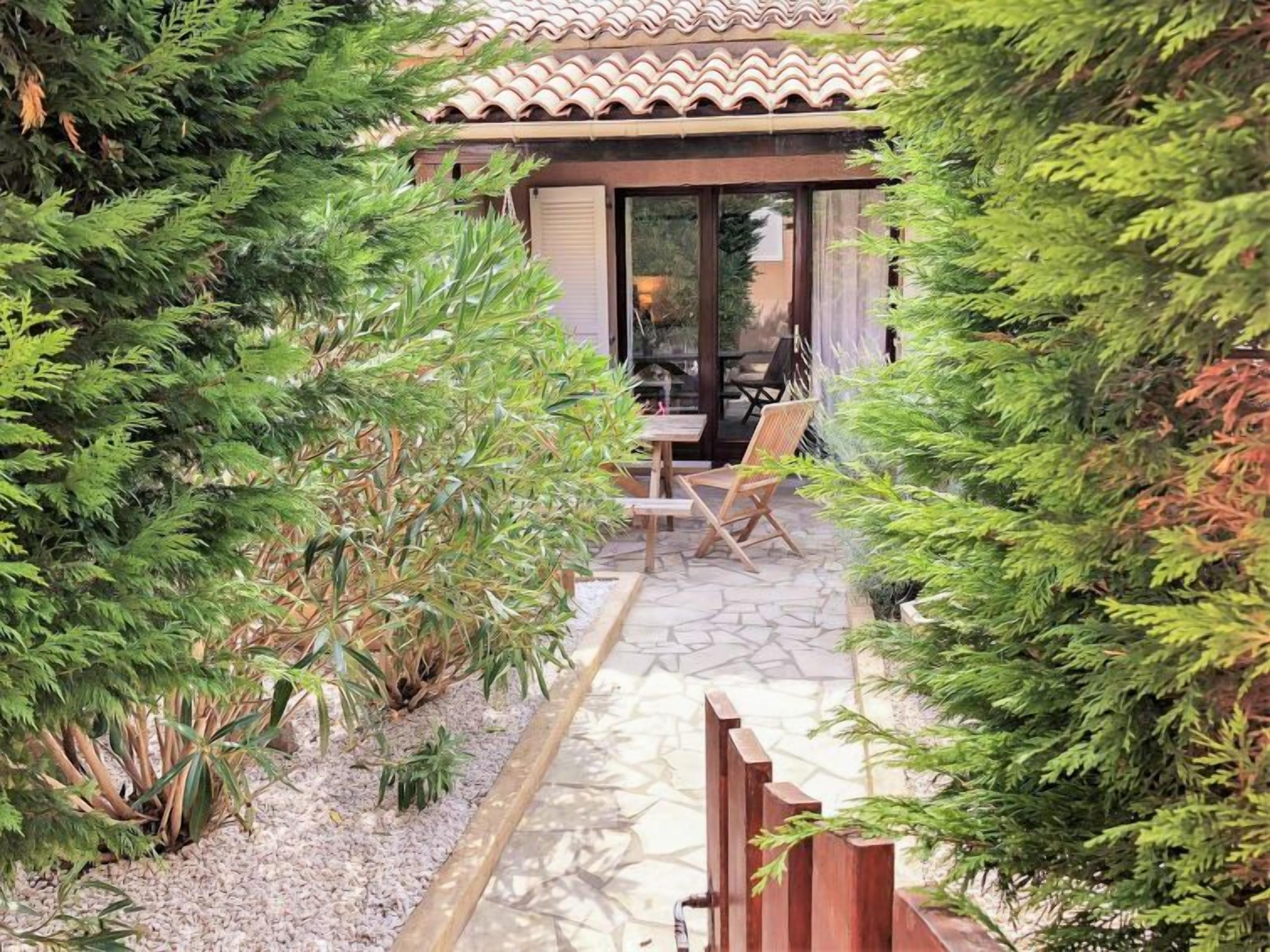 A patio area with a table and chairs, surrounded by greenery and a tiled roof structure.
