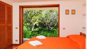 Une chambre avec une couvre-lit orange, une porte en bois et une vue sur les arbres à travers une porte vitrée.