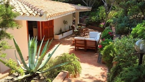 Une maison avec un toit en tuiles, une terrasse avec une table et des chaises, et diverses plantes.