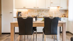 A modern kitchen with white cabinets, a wooden dining table, and black chairs. - Haus Adora by Interhome (Saas-Almagell)