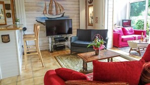 Una sala de estar con una televisión, un sofá rojo, un sofá rosa y un ventanal grande.