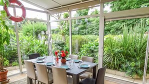 Un comedor estilo invernadero con una mesa preparada para seis personas, rodeado de sillas, y vistas a abundante vegetación.