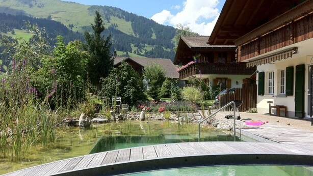 Ein Poolbereich mit Holzterrasse, umgeben von üppiger Vegetation und einem Blick auf die Berge.