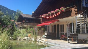 Ein traditionelles Chalet mit einer Holzdiele, einem kleinen Teich und Bergblick.