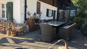 Eine Terrassengruppe mit Korbmöbeln, einem Steinbrunnen und einer rustikalen Holzvitrine.