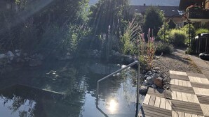 Ein friedlicher Garten mit einer Holzterrasse, einem kleinen Teich und Bergblick.
