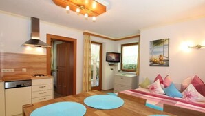 A compact living space with a wooden dining table, a sofa with patterned cushions, a television, and a kitchen area with a stove and cabinets. - Apartment Anita by Interhome (Zell am Ziller)