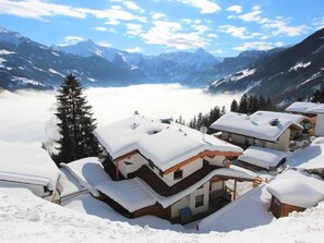 Un pueblo cubierto de nieve con edificios de estilo chalet, cielo despejado y vistas a montañas distantes.