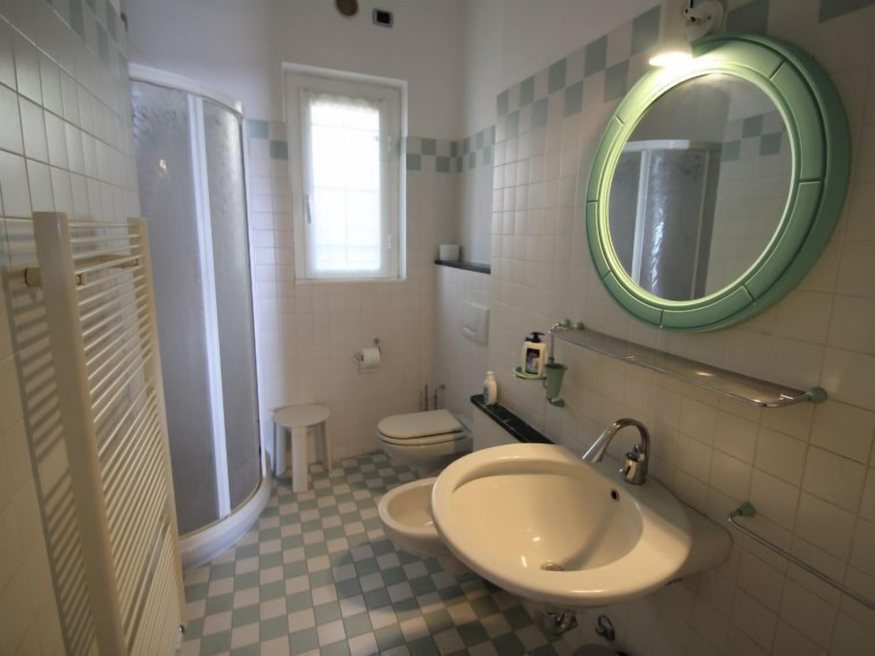 A bathroom with a checkered floor, a sink, a toilet, a mirror, and a window.