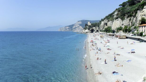Ein Strand mit klarem, blauem Wasser, Menschen, die sich sonnen, und Gebäuden auf einer Klippe.