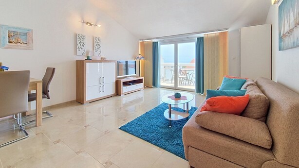 A modern apartment with a dining area, a living room with a sofa, a TV, and a balcony with a view.