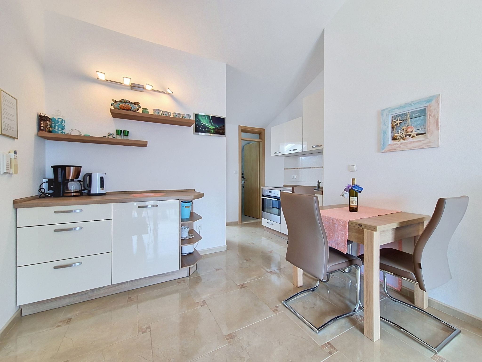 A modern kitchen with a dining area, featuring a coffee maker, a wine bottle, and a TV on the wall.
