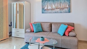 A modern living room with a sofa, glass coffee table, and a painting of sailboats on the wall.