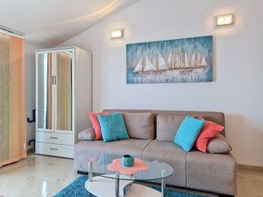 Un salon moderne avec un canapé, une table basse en verre et un tableau représentant des voiliers accroché au mur.