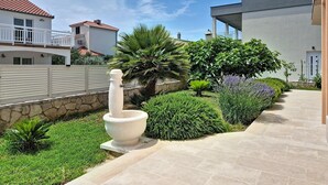 A residential area with a stone wall, a white bollard, and a variety of green shrubs and plants.
