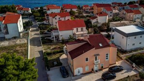 A coastal residential area with houses featuring red roofs and white walls, a clear view of the sea, and a parking area with cars.