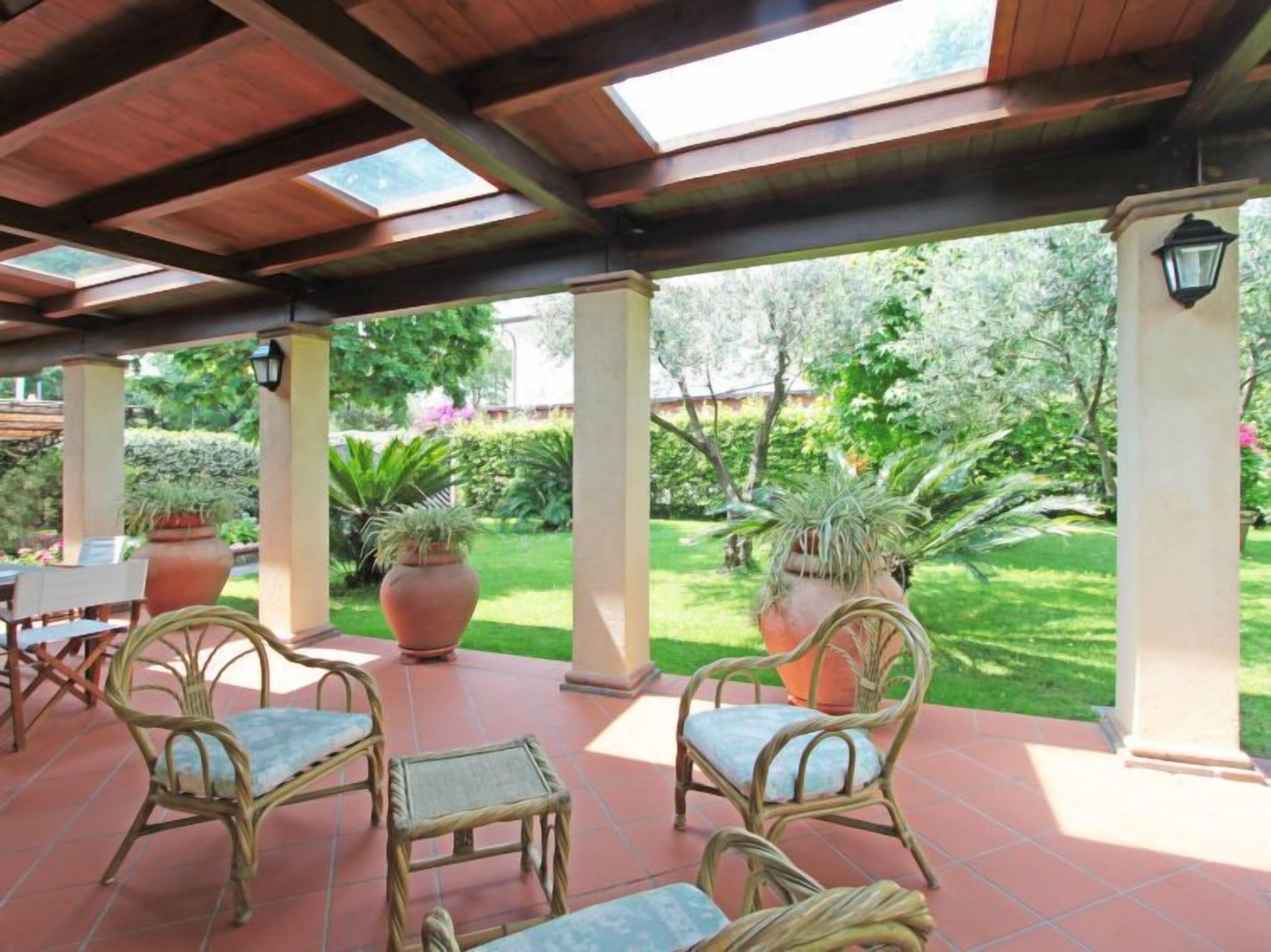 Eine Terrasse im Freien mit Korbstühlen, Terrakotta-Pflanzgefäßen und Blick auf einen gepflegten Garten.