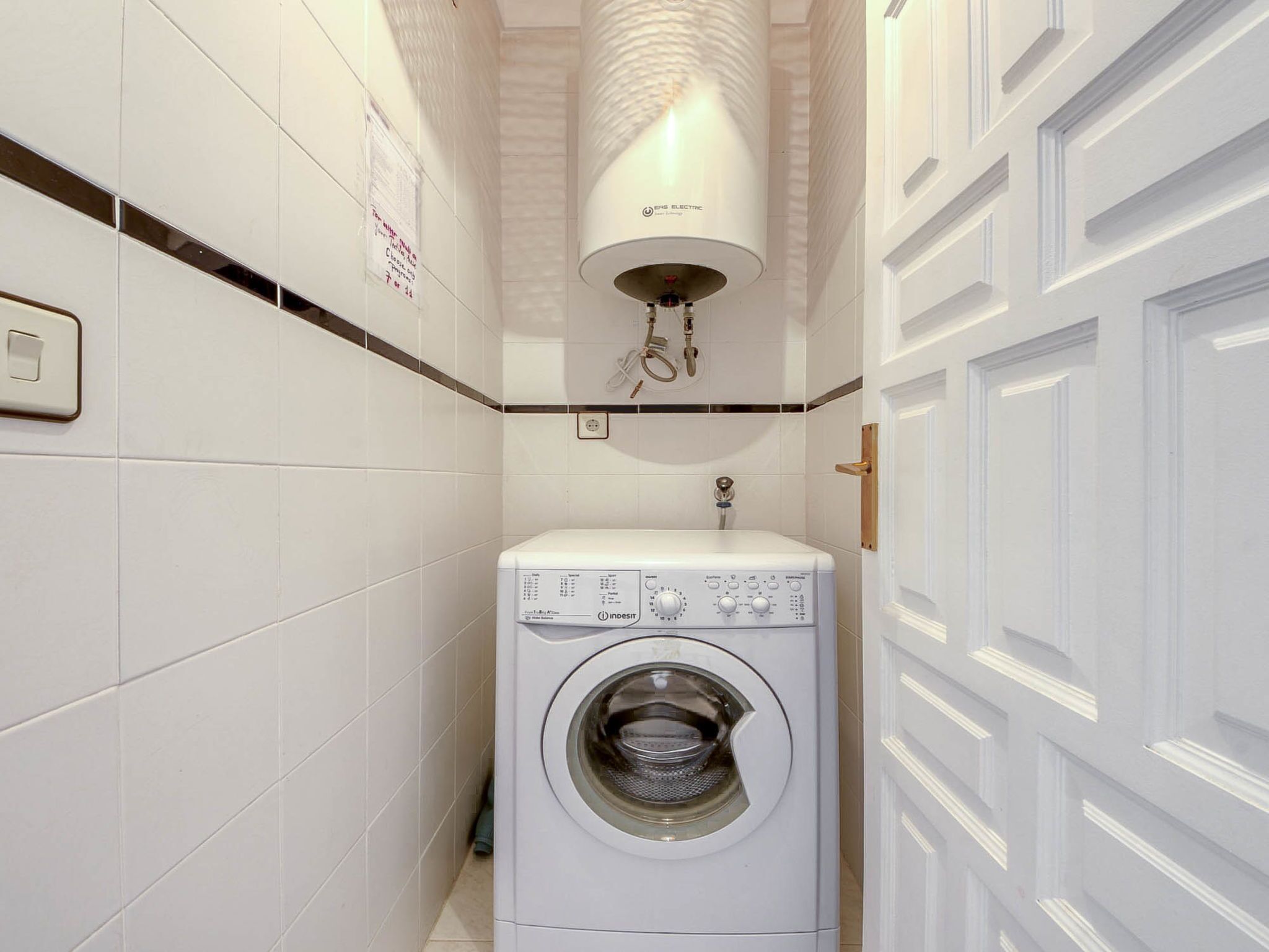 A compact laundry room with a front-loading washing machine, a sink, and a wall-mounted heater.