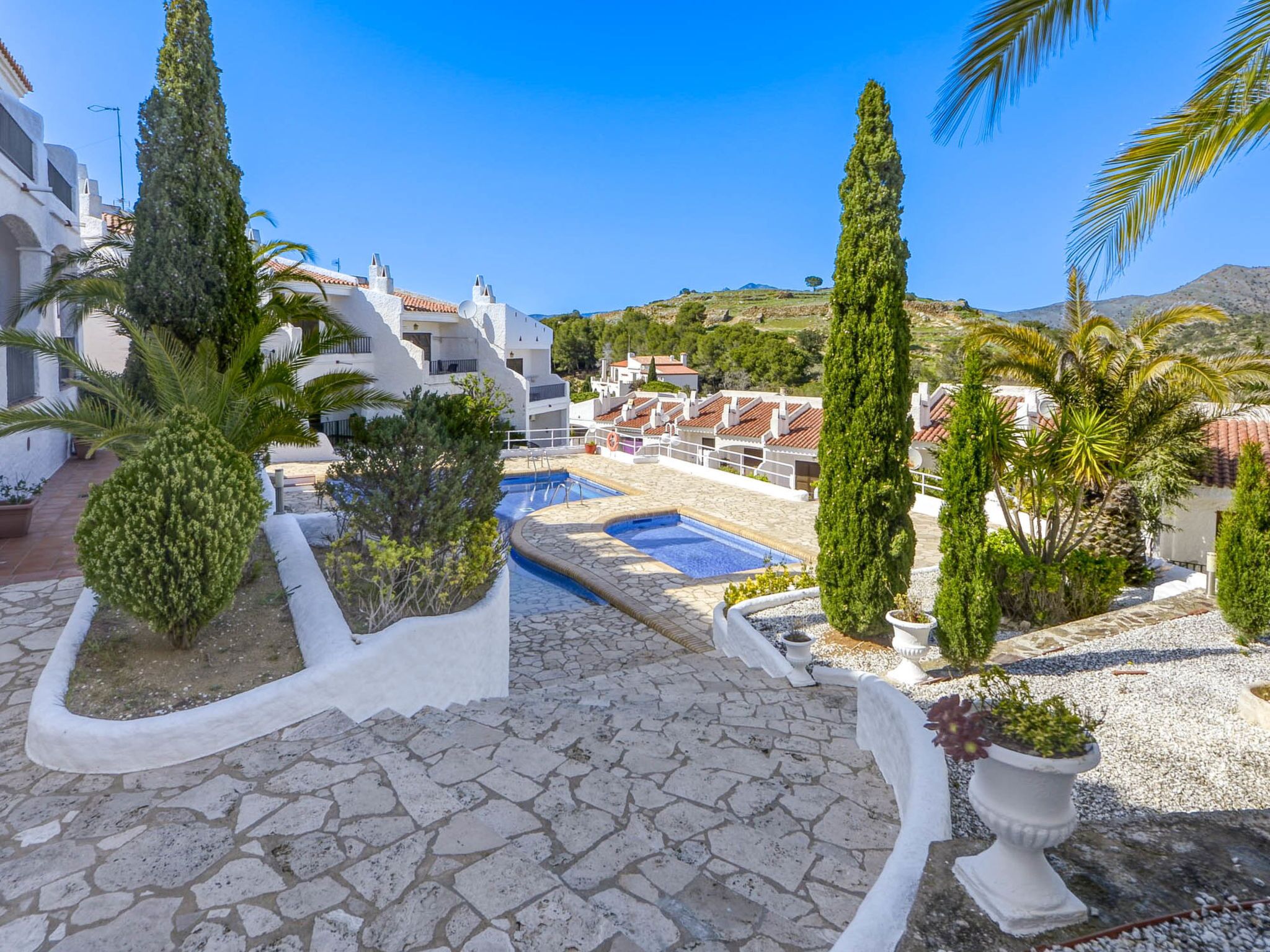 A rooftop pool area with stone flooring, surrounded by white walls and potted plants.