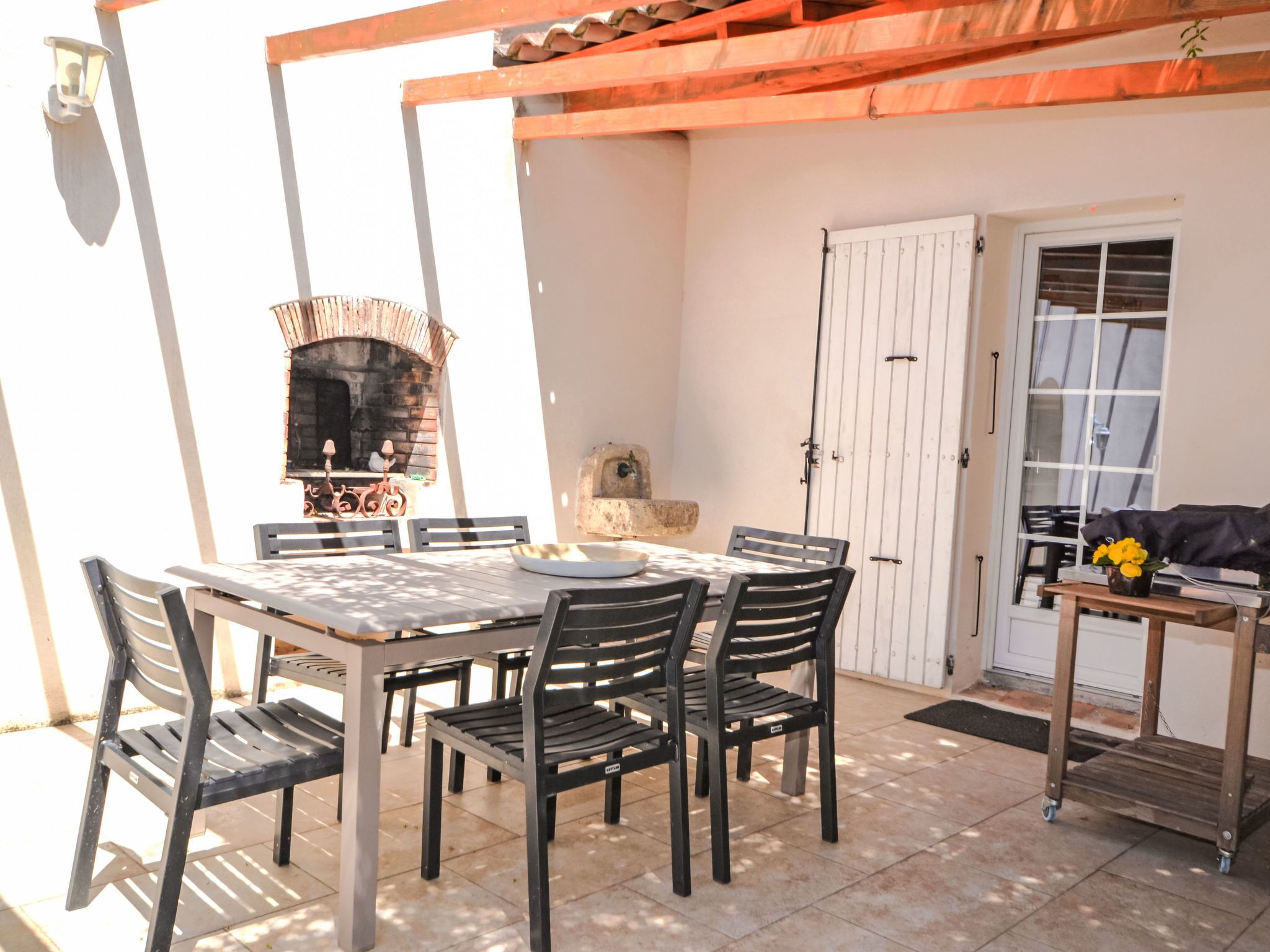 Un patio exterior con una mesa, sillas, una chimenea de ladrillo y un ventanal corredera.