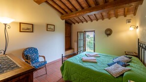 Ein Schlafzimmer mit Holzbalkendecke, einer grünen Tagesdecke, einem Stuhl, einem Schreibtisch und einem Fenster mit Blick.
