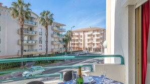 A balcony with a table set for two, overlooking a street with cars and palm trees. - Apartment L'Open by Interhome (Fréjus)
