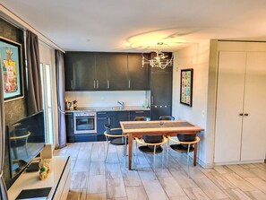 A modern kitchen with dark cabinets, a central island, and a dining area with a wooden table and chairs. - Collina Verde B by Interhome (Ascona)
