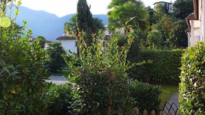 A lush garden with various plants and trees, a pathway, and a view of distant mountains. - Collina Verde B by Interhome (Ascona)