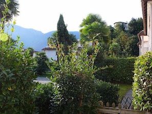 A lush garden with various plants and trees, a pathway, and a view of distant mountains.