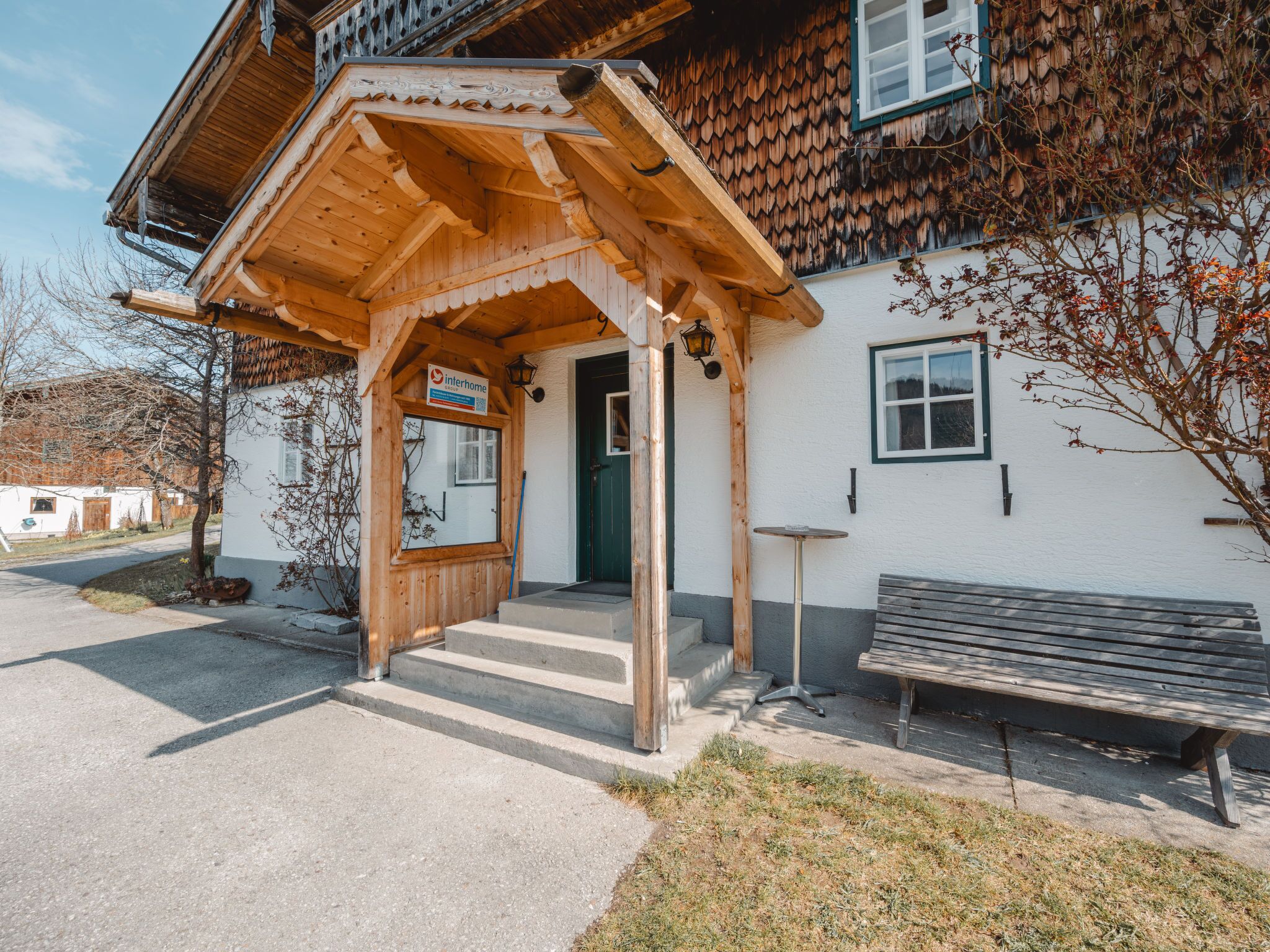 A wooden building with a covered entrance, a bench, and a sign indicating it is a home.