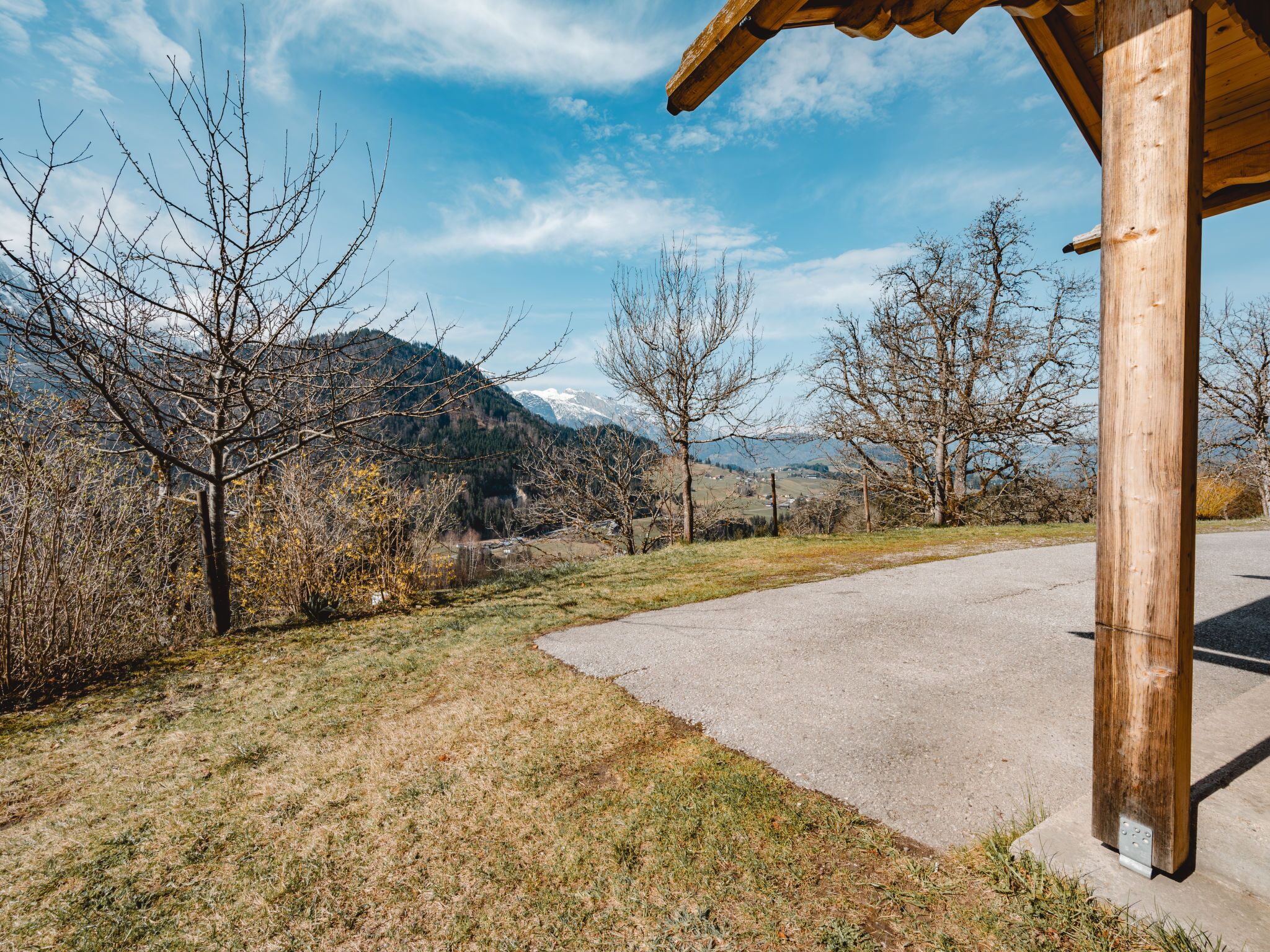 A rural road curving through a landscape with mountains in the background, a wooden structure on the right, and sparse vegetation.