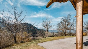 Un camino rural serpentea por un paisaje con montañas al fondo, una estructura de madera a la derecha y vegetación escasa.
