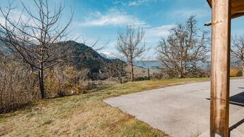 A rural road curving through a landscape with mountains in the background, a wooden structure on the right, and sparse vegetation.