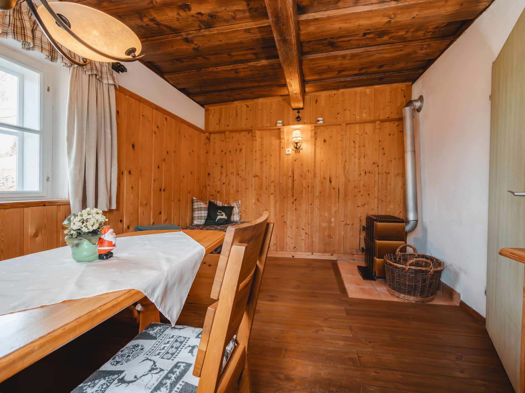 A wooden cabin interior with a dining table, chairs, a bench, a fireplace, and a window with curtains.