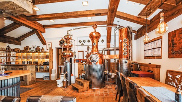 Un interior rústico con vigas de madera a la vista, una zona de bar con estantes llenos de botellas y un área de descanso con sillones de cuero.