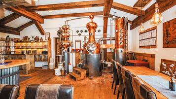 A rustic interior with exposed wooden beams, a bar area with shelves of bottles, and a seating area with leather chairs.