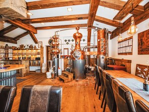 A rustic interior with exposed wooden beams, a bar area with shelves of bottles, and a seating area with leather chairs.