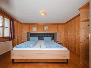 Ein Schlafzimmer mit Holzwänden, einem Bett, einem Fenster mit Vorhängen und einem Heizkörper.